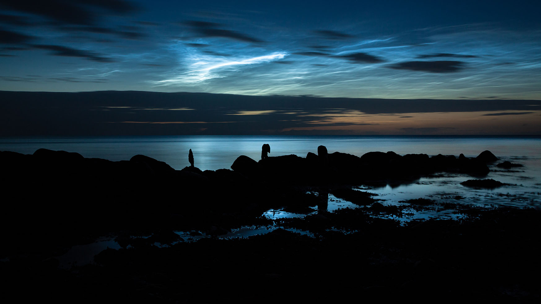 Leuchtende Nachtwolken über der Silhouette einer Buhne an der Kieler Außenförde
