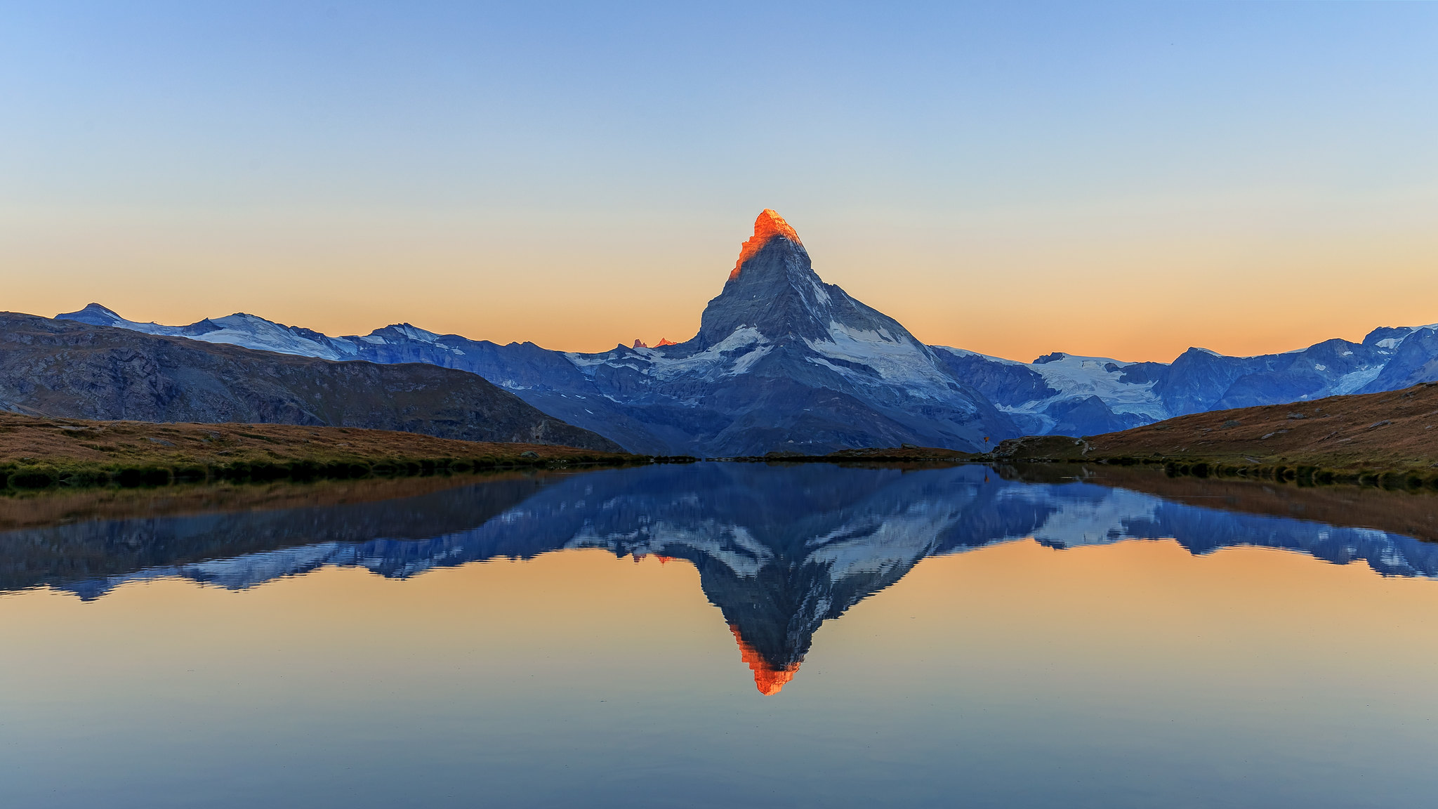 Foto vom Matterhorn mit goldgelber Beleuchtung vom Sonnenaufgang und
Spiegelung in einem See